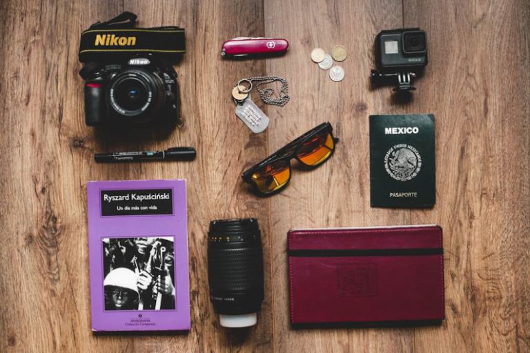Travel Essentials - a table topped with a camera, passport, sunglasses and other items
