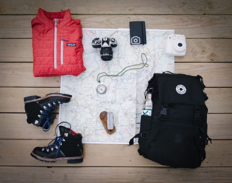 Travel Gear - black hiking backpack near white Fujifilm instax mini camera near black leather boots, red half-zip jacket, gray pocket watch on white map