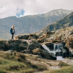 Breathtaking Views - a woman standing on top of a mountain next to a waterfall
