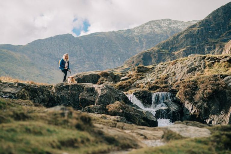 Breathtaking Views - a woman standing on top of a mountain next to a waterfall