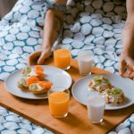 Romantic Bed And Breakfast - person serving pastries on white ceramic plates with fruit juice glasses on wooden tray on top of bed