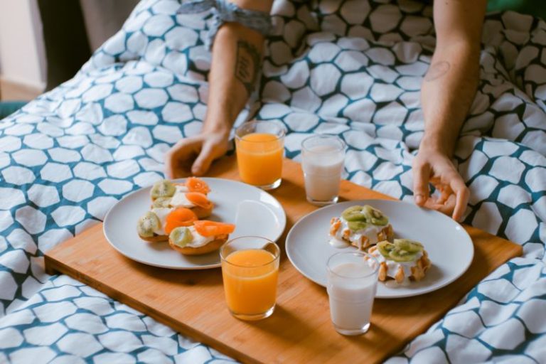 Romantic Bed And Breakfast - person serving pastries on white ceramic plates with fruit juice glasses on wooden tray on top of bed