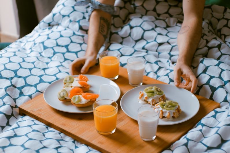Romantic Bed And Breakfast - person serving pastries on white ceramic plates with fruit juice glasses on wooden tray on top of bed