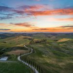 Tuscany Landscape - road between green grass field near mountains under blue and brown sky at golden hour