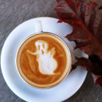 Halloween B&B - white ceramic teacup filled with ghost illustration coffee latte on white ceramic saucer beside maroon leaf photography